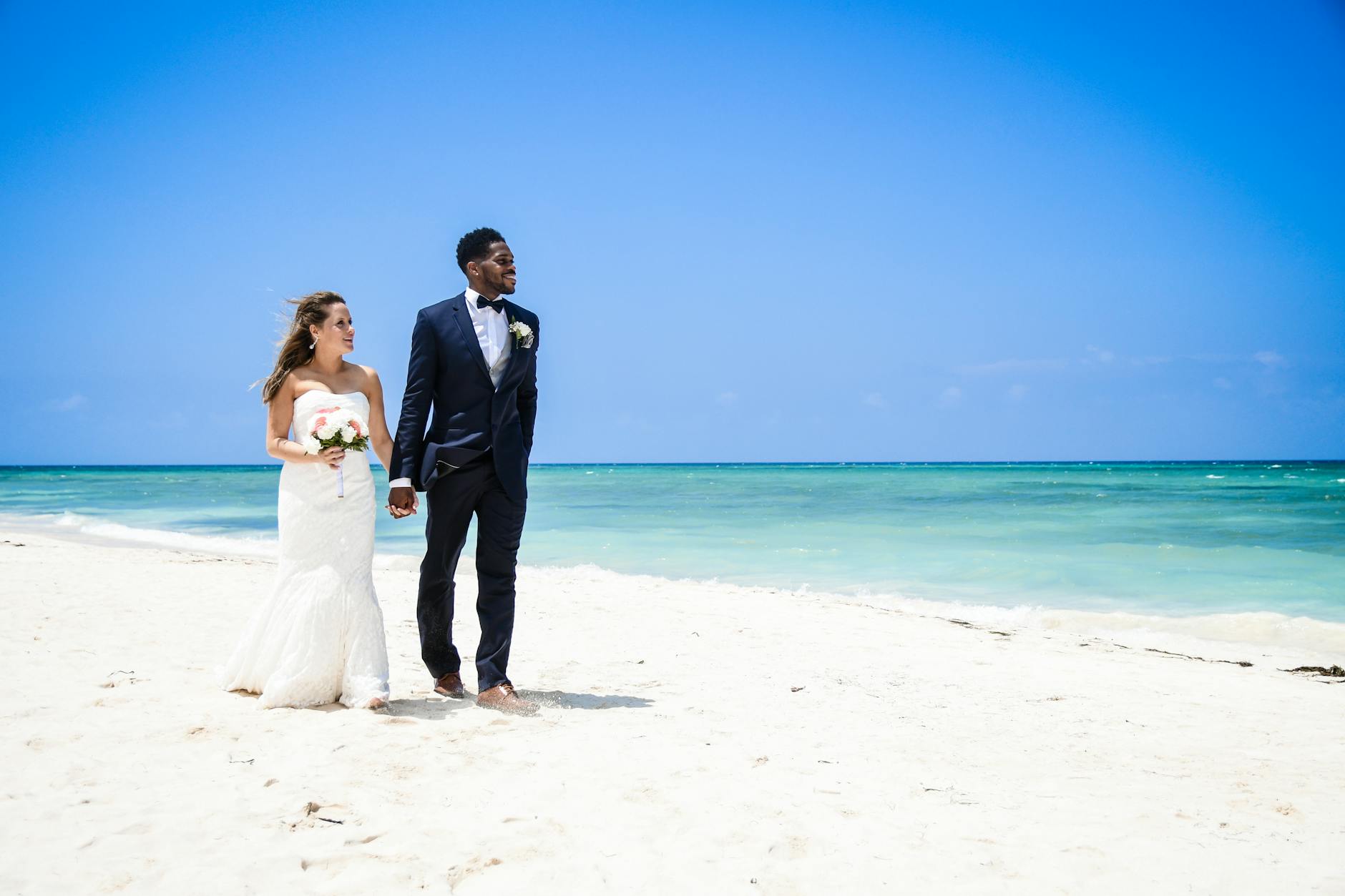 A bride and groom walking hand-in-hand on a white-sand tropical beach