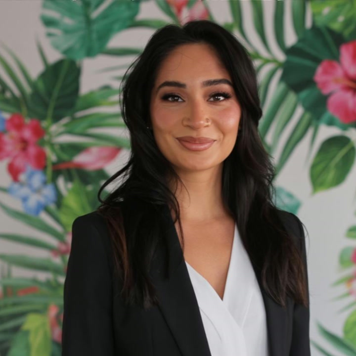 Jas, content creator for Destinations by Easy Weddings, in a tailored black blazer against a tropical floral backdrop
